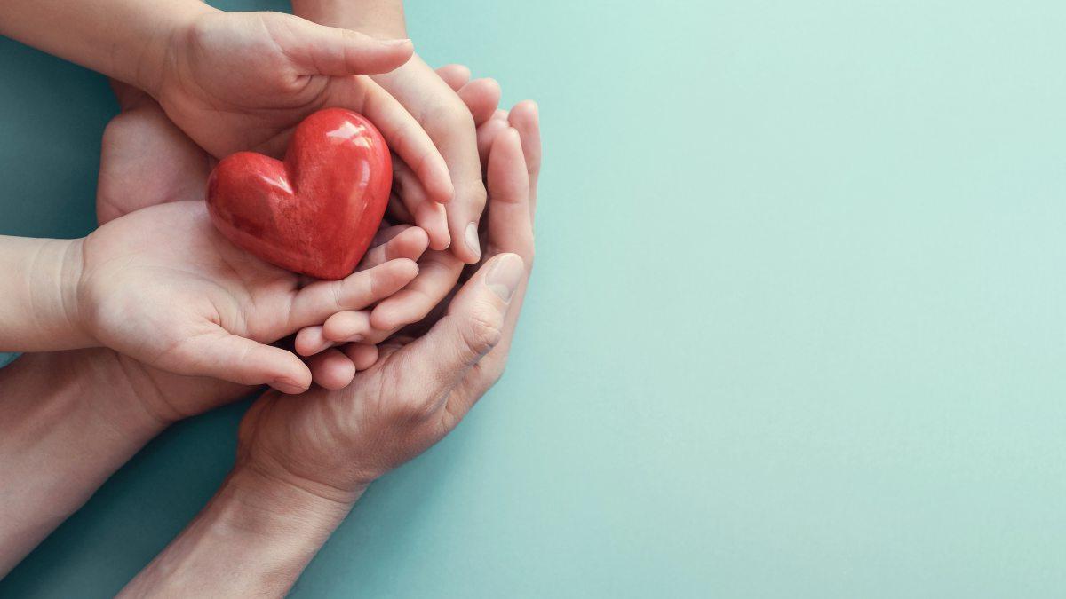 Adult and child hands holding red heart on aqua background.